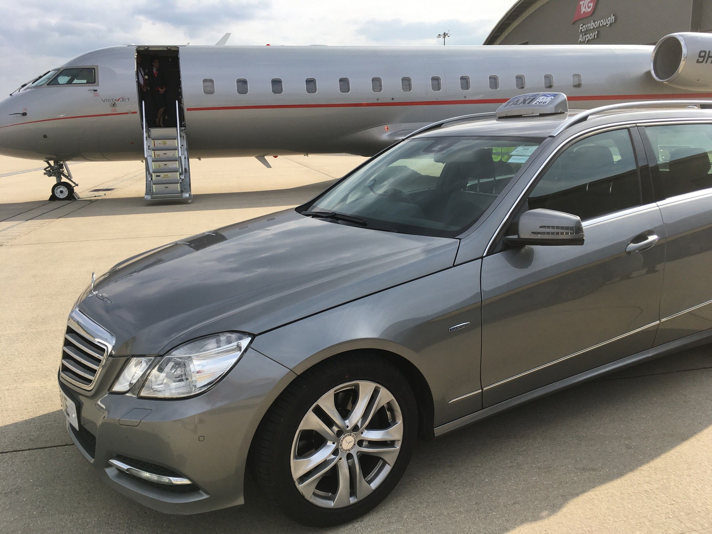 Silver Mercedes-Benz E-Class estate beside a private jet on an airfield apron
